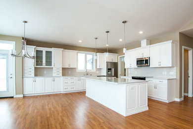 Inspiration for a huge transitional l-shaped vinyl floor and brown floor eat-in kitchen remodel in Calgary with an undermount sink, raised-panel cabinets, white cabinets, quartz countertops, white backsplash, subway tile backsplash, stainless steel appliances and an island