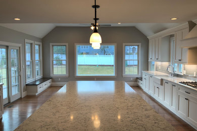 Inspiration for a huge timeless single-wall medium tone wood floor and brown floor open concept kitchen remodel in Boston with a farmhouse sink, beaded inset cabinets, white cabinets, quartz countertops, gray backsplash, ceramic backsplash, stainless steel appliances, an island and gray countertops