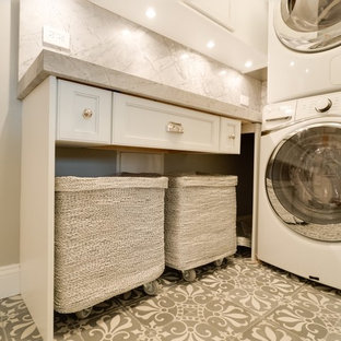 Photo of a small classic l-shaped utility room in New York with white cabinets, marble worktops, grey walls, concrete flooring, a stacked washer and dryer, grey floors, grey worktops and recessed-panel cabinets.