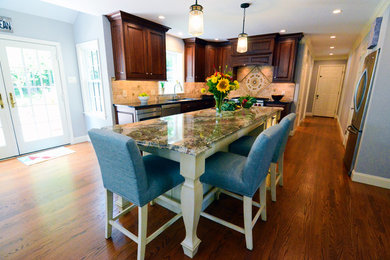 Example of a large transitional l-shaped dark wood floor and brown floor eat-in kitchen design in Philadelphia with an undermount sink, raised-panel cabinets, medium tone wood cabinets, granite countertops, beige backsplash, travertine backsplash, stainless steel appliances and an island