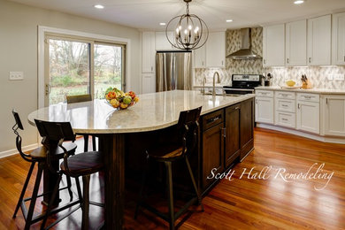 Example of a large classic single-wall medium tone wood floor and brown floor eat-in kitchen design in Columbus with an undermount sink, shaker cabinets, white cabinets, white backsplash, ceramic backsplash, stainless steel appliances, an island, multicolored countertops and quartz countertops