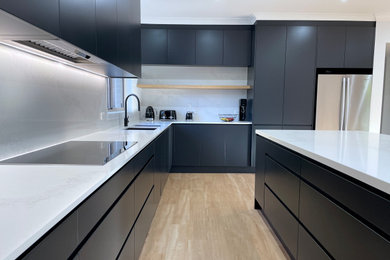 Design ideas for a large l-shaped open plan kitchen in Sydney with an undermount sink, flat-panel cabinets, black cabinets, quartz benchtops, white splashback, engineered quartz splashback, black appliances, light hardwood floors, with island, brown floor and white benchtop.