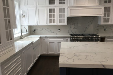 Kitchen - large modern dark wood floor and brown floor kitchen idea in Chicago with a farmhouse sink, recessed-panel cabinets, white cabinets, quartz countertops, white backsplash, stone slab backsplash, stainless steel appliances, an island and white countertops