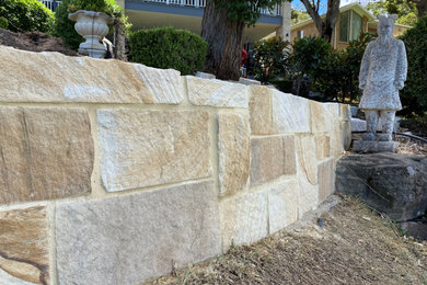 This is an example of a mid-sized traditional backyard partial sun formal garden in Sydney with a retaining wall, natural stone pavers and a stone fence.
