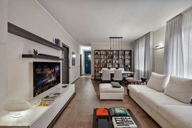 Imagen de biblioteca en casa abierta actual de tamaño medio con paredes beige, suelo de madera clara, televisor colgado en la pared y suelo beige