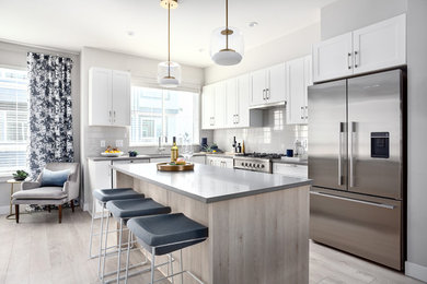 Kitchen - coastal l-shaped light wood floor and gray floor kitchen idea in Vancouver with an undermount sink, shaker cabinets, white cabinets, gray backsplash, stainless steel appliances, an island and gray countertops