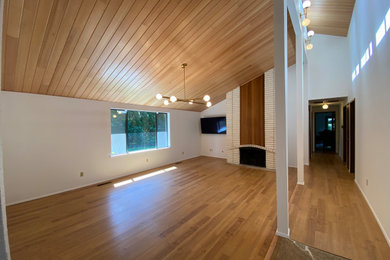 Diseño de sala de estar retro de tamaño medio con paredes blancas, suelo de madera clara, todas las chimeneas, marco de chimenea de ladrillo y madera