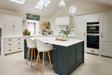Classic kitchen/diner in Essex with a belfast sink, shaker cabinets, green cabinets, quartz worktops, white splashback, black appliances, porcelain flooring, an island, grey floors, white worktops and a vaulted ceiling.