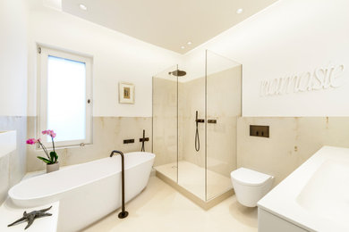 Mid-sized traditional bathroom in Cologne with a freestanding tub, a wall-mount toilet, beige tile, beige floor, flat-panel cabinets, white cabinets, an open shower, ceramic tile, beige walls, an integrated sink, solid surface benchtops, an open shower and white benchtops.