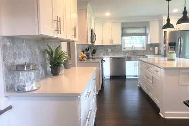 Photo of a large modern eat-in kitchen in Detroit with a farmhouse sink, shaker cabinets, white cabinets, grey splashback, stainless steel appliances, dark hardwood floors, with island, brown floor and white benchtop.
