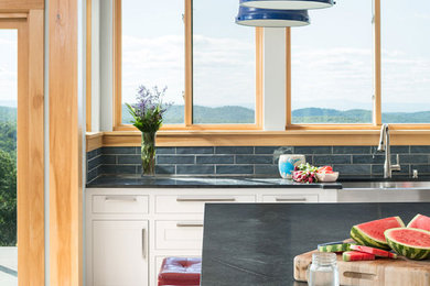 Example of a huge farmhouse l-shaped light wood floor and brown floor kitchen design in Burlington with white cabinets, an island and gray countertops
