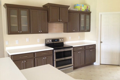 Enclosed kitchen - mid-sized contemporary l-shaped linoleum floor enclosed kitchen idea in Miami with flat-panel cabinets, brown cabinets, solid surface countertops, white backsplash, stainless steel appliances and no island