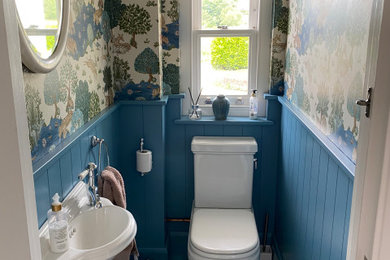 Photo of a small traditional cloakroom in Kent with beige floors, a feature wall, panelled walls, blue cabinets, a two-piece toilet, blue walls, porcelain flooring, a wall-mounted sink and a floating vanity unit.