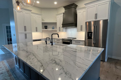 Example of a huge minimalist l-shaped vinyl floor and brown floor eat-in kitchen design in Indianapolis with a farmhouse sink, shaker cabinets, quartz countertops, white backsplash, subway tile backsplash, stainless steel appliances, an island and white countertops