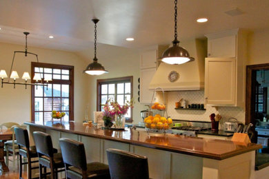 Example of a mid-sized classic l-shaped medium tone wood floor and brown floor eat-in kitchen design in Los Angeles with an undermount sink, flat-panel cabinets, beige cabinets, granite countertops, white backsplash, glass tile backsplash, stainless steel appliances and an island