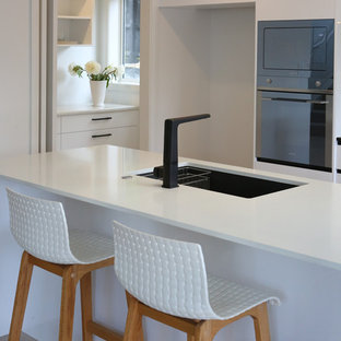 Large kitchen pantry pictures - Kitchen pantry - large galley laminate floor and multicolored floor kitchen pantry idea in Auckland with an undermount sink, flat-panel cabinets, white cabinets, quartz countertops, black backsplash, glass sheet backsplash, stainless steel appliances and an island