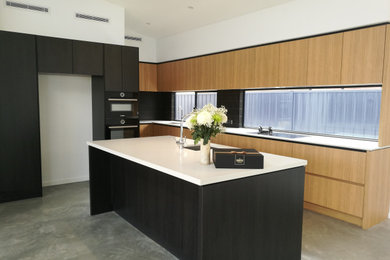 This is an example of a mid-sized contemporary l-shaped open plan kitchen in Perth with an undermount sink, flat-panel cabinets, medium wood cabinets, quartz benchtops, black splashback, ceramic splashback, stainless steel appliances, concrete floors, with island, grey floor and white benchtop.