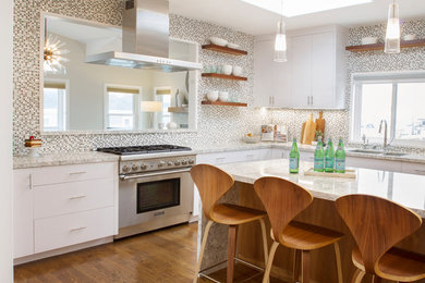 Beach style u-shaped eat-in kitchen with with island, brown floor, white benchtop, a double-bowl sink, mosaic tile splashback, stainless steel appliances, medium hardwood floors, flat-panel cabinets, white cabinets, multi-coloured splashback and quartz benchtops.