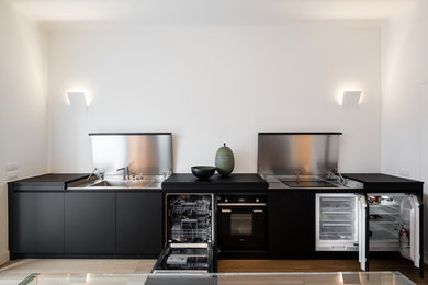 Design ideas for a contemporary single-wall eat-in kitchen in Milan with a single-bowl sink, black cabinets, stainless steel benchtops, stainless steel appliances, light hardwood floors, no island, brown floor and black benchtop.