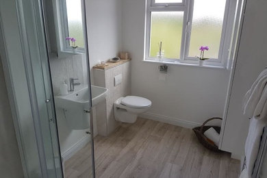 Photo of a contemporary ensuite bathroom in Surrey with a corner shower, a wall mounted toilet, white walls, laminate floors, a wall-mounted sink, brown floors and a sliding door.