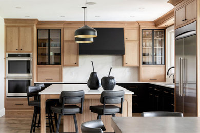 This is an example of a large transitional u-shaped eat-in kitchen in Toronto with flat-panel cabinets, light wood cabinets, quartz benchtops, white splashback, engineered quartz splashback, stainless steel appliances, with island, brown floor and white benchtop.