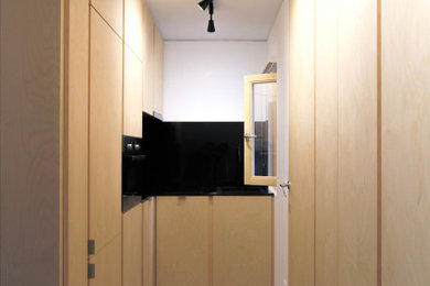 Imagen de cocinas en L nórdica pequeña abierta sin isla con fregadero de un seno, armarios con paneles lisos, puertas de armario de madera clara, encimera de granito, salpicadero negro, salpicadero de metal, electrodomésticos con paneles, suelo de cemento, suelo gris y encimeras negras