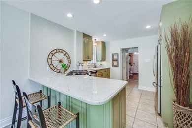 Mid-sized mid-century modern l-shaped ceramic tile and beige floor eat-in kitchen photo in Philadelphia with an undermount sink, raised-panel cabinets, green cabinets, solid surface countertops, white backsplash, stone tile backsplash, stainless steel appliances, an island and white countertops