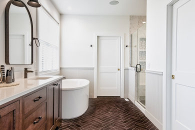 Example of a cottage chic master ceramic tile, brown floor, double-sink and wainscoting bathroom design in Other with flat-panel cabinets, medium tone wood cabinets, white walls, an undermount sink, quartz countertops, a hinged shower door, white countertops and a built-in vanity