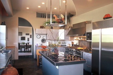 Inspiration for a large industrial l-shaped slate floor and brown floor enclosed kitchen remodel in Phoenix with flat-panel cabinets, gray cabinets, tile countertops, an island, a double-bowl sink, gray backsplash, stainless steel appliances and black countertops