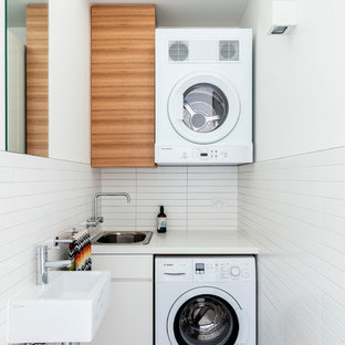 シドニーの中サイズのコンテンポラリースタイルのおしゃれなランドリールーム (フラットパネル扉のキャビネット、中間色木目調キャビネット、白い壁、上下配置の洗濯機・乾燥機、黒い床、白いキッチンカウンター) の写真