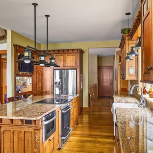 Mittelgroße Rustikale Küche in L-Form mit Vorratsschrank, Landhausspüle, flächenbündigen Schrankfronten, hellbraunen Holzschränken, Granit-Arbeitsplatte, Küchenrückwand in Beige, Rückwand aus Steinfliesen, Küchengeräten aus Edelstahl, braunem Holzboden und Kücheninsel in New York