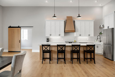 Inspiration for a mid-sized modern l-shaped eat-in kitchen in Minneapolis with an undermount sink, shaker cabinets, white cabinets, quartzite benchtops, stainless steel appliances, laminate floors, with island, brown floor and white benchtop.