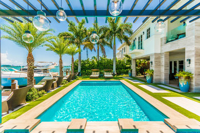 Photo of a large contemporary backyard rectangular lap pool in Miami with natural stone pavers.