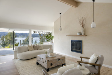 Example of a mid-sized beach style open concept medium tone wood floor, brown floor and vaulted ceiling living room design in Seattle with white walls, a standard fireplace, a plaster fireplace and no tv
