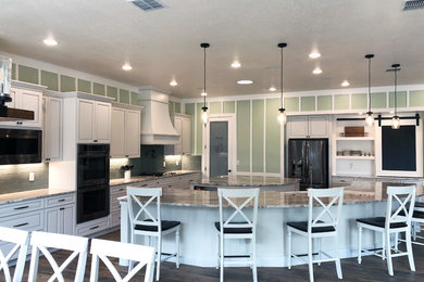 Open concept kitchen - huge farmhouse l-shaped ceramic tile and brown floor open concept kitchen idea in Austin with a farmhouse sink, raised-panel cabinets, white cabinets, granite countertops, green backsplash, glass tile backsplash, stainless steel appliances, two islands and multicolored countertops