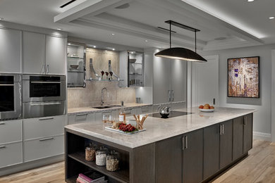 Example of a trendy galley light wood floor and beige floor kitchen design in Chicago with an undermount sink, flat-panel cabinets, gray cabinets, beige backsplash, stone slab backsplash, paneled appliances, an island and beige countertops