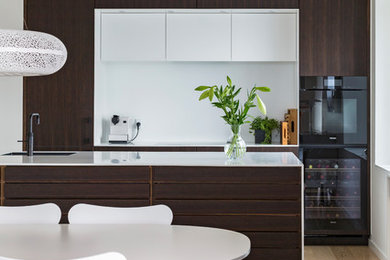 This is an example of a mid-sized scandinavian galley open plan kitchen in Aalborg with an undermount sink, flat-panel cabinets, dark wood cabinets, black appliances, with island and white benchtop.