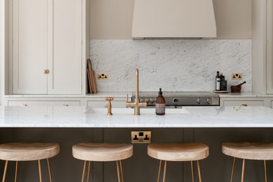 Inspiration for a large classic single-wall open plan kitchen in London with a built-in sink, shaker cabinets, light wood cabinets, marble worktops, white splashback, marble splashback, black appliances, limestone flooring, an island, beige floors, white worktops, a vaulted ceiling and feature lighting.