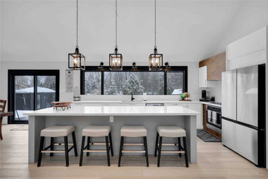 Eat-in kitchen - large coastal l-shaped light wood floor, brown floor and vaulted ceiling eat-in kitchen idea in Philadelphia with an undermount sink, flat-panel cabinets, white cabinets, solid surface countertops, white backsplash, subway tile backsplash, stainless steel appliances, an island and white countertops