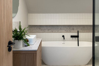 Design ideas for a medium sized contemporary grey and brown bathroom in Kent with flat-panel cabinets, medium wood cabinets, a freestanding bath, a corner shower, a wall mounted toilet, white tiles, ceramic tiles, terracotta flooring, a console sink, marble worktops, grey floors, an open shower, grey worktops, a wall niche, a single sink, a freestanding vanity unit and a vaulted ceiling.