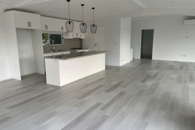 Photo of a large modern l-shaped open plan kitchen in Sydney with a drop-in sink, white cabinets, beige splashback, stainless steel appliances, laminate floors, with island, grey floor, beige benchtop and exposed beam.