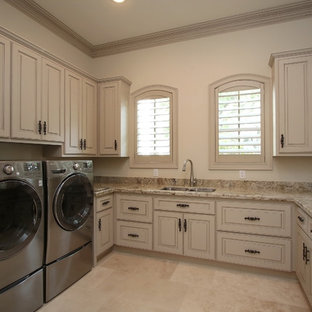Design ideas for a large traditional u-shaped utility room in Houston with a double-bowl sink, raised-panel cabinets, granite worktops, travertine flooring, a side by side washer and dryer and beige floors.