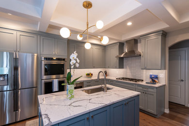 Medium sized traditional u-shaped kitchen/diner in Denver with a submerged sink, shaker cabinets, blue cabinets, engineered stone countertops, white splashback, ceramic splashback, stainless steel appliances, laminate floors, an island, brown floors, white worktops and a coffered ceiling.
