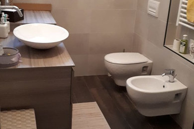 This is an example of a small modern 3/4 bathroom with light wood cabinets, a curbless shower, a wall-mount toilet, beige tile, porcelain tile, white walls, porcelain floors, a vessel sink, brown floor, an open shower and brown benchtops.