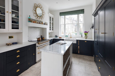 Photo of a small transitional l-shaped eat-in kitchen in London with a farmhouse sink, shaker cabinets, black cabinets, quartzite benchtops, limestone floors, with island, beige floor, white splashback and white appliances.