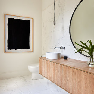 Powder room - large contemporary white tile and marble tile marble floor and white floor powder room idea in Charlotte with flat-panel cabinets, light wood cabinets, white walls, a vessel sink, wood countertops and beige countertops