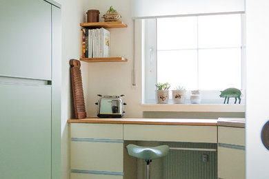 Kleine Moderne Küche ohne Insel in L-Form mit Waschbecken, flächenbündigen Schrankfronten, beigen Schränken, Arbeitsplatte aus Holz, Küchenrückwand in Grün, Glasrückwand, Küchengeräten aus Edelstahl, Linoleum und braunem Boden in Sonstige