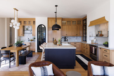Inspiration for a transitional l-shaped medium tone wood floor and brown floor kitchen remodel in Other with an undermount sink, shaker cabinets, medium tone wood cabinets, gray backsplash, stainless steel appliances, two islands and white countertops