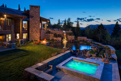 Photo of an expansive country backyard round natural pool in Other with a hot tub and natural stone pavers.