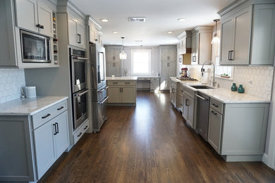 Design ideas for a large transitional u-shaped eat-in kitchen in Providence with an undermount sink, recessed-panel cabinets, grey cabinets, quartz benchtops, white splashback, ceramic splashback, stainless steel appliances, medium hardwood floors, with island, brown floor and white benchtop.